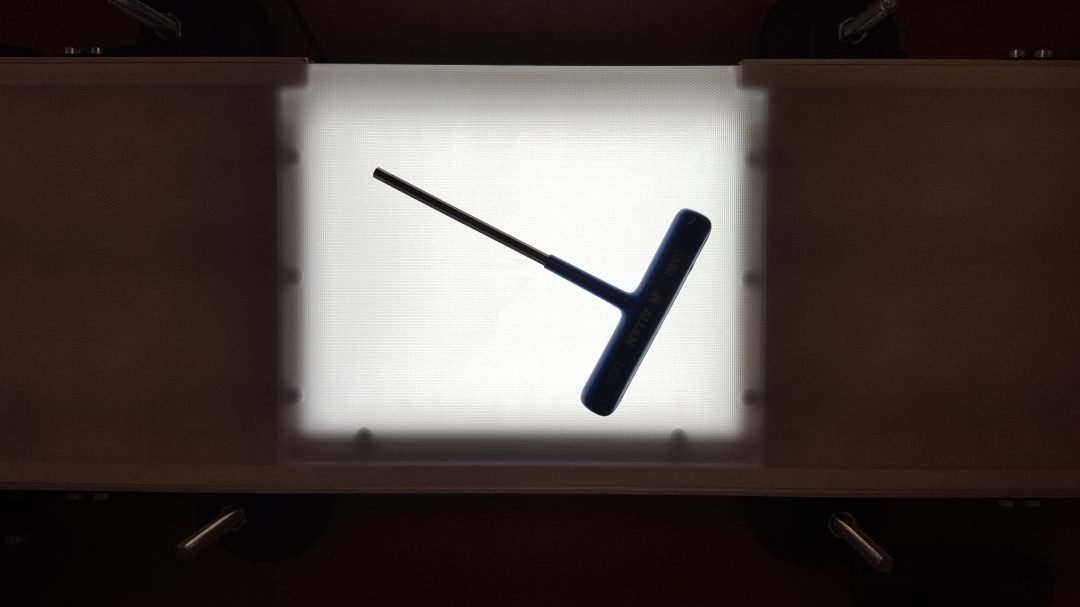 Inspection tool silhouetted above an illuminated conveyor section