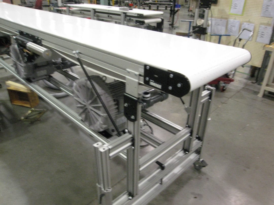 Vacuum belt conveyor holding flat product to the belt surface